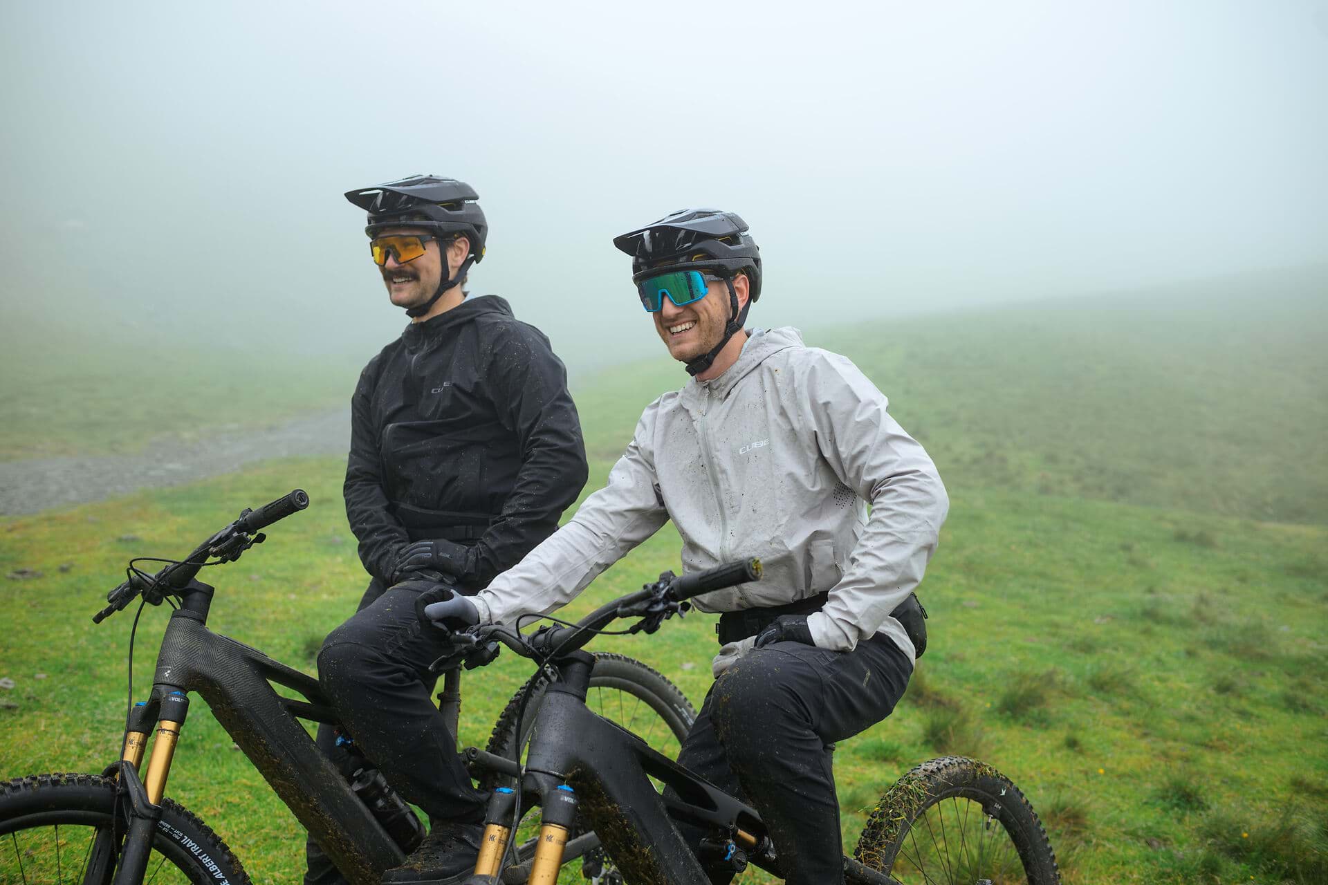 Zwei Radfahrer stehen nebeneinander auf einer Almwiese im Nebel